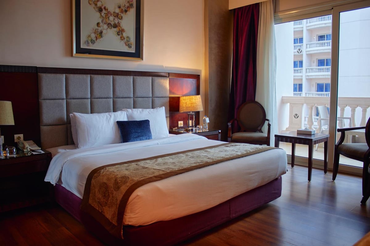 Tolip Hotel Alexandria bedroom with a padded headboard and balcony doors.