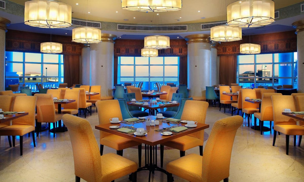 Tolip Hotel Alexandria restaurant with orange upholstered chairs and large windows.