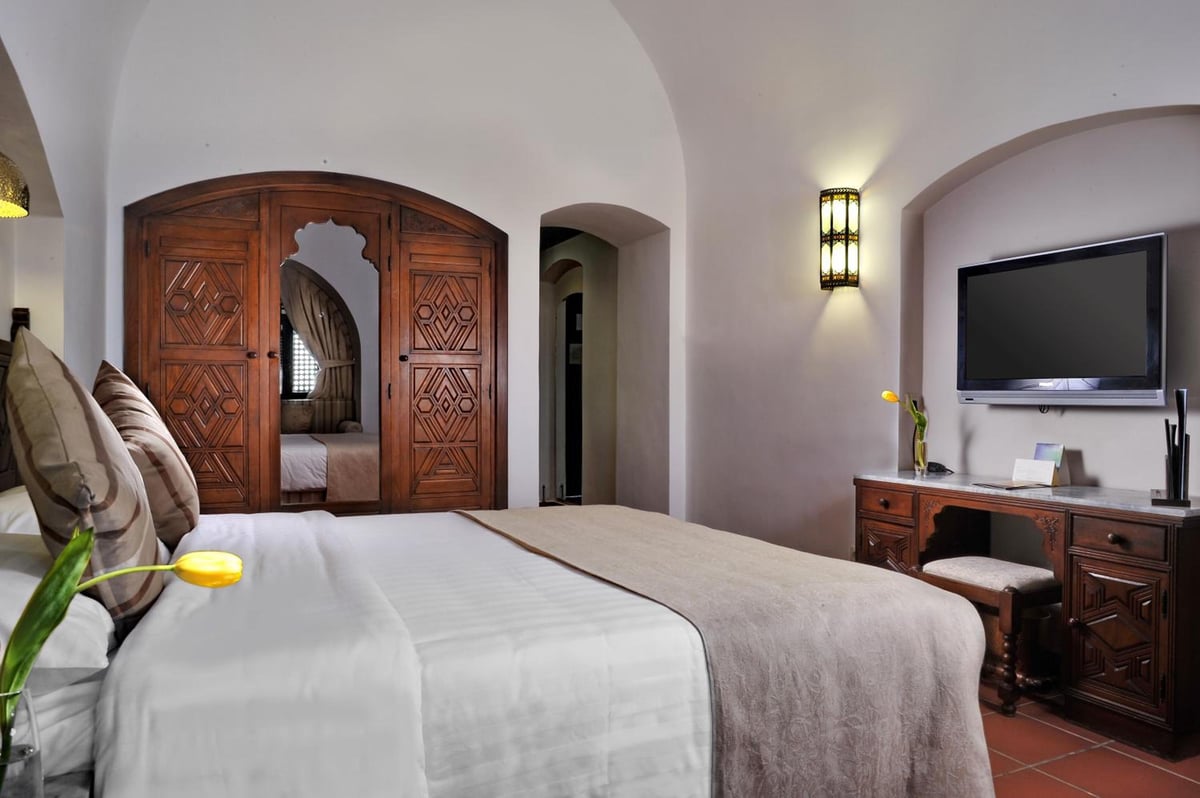 Movenpick Resort Sharm El Sheikh bedroom with a bed and carved wooden wardrobe.