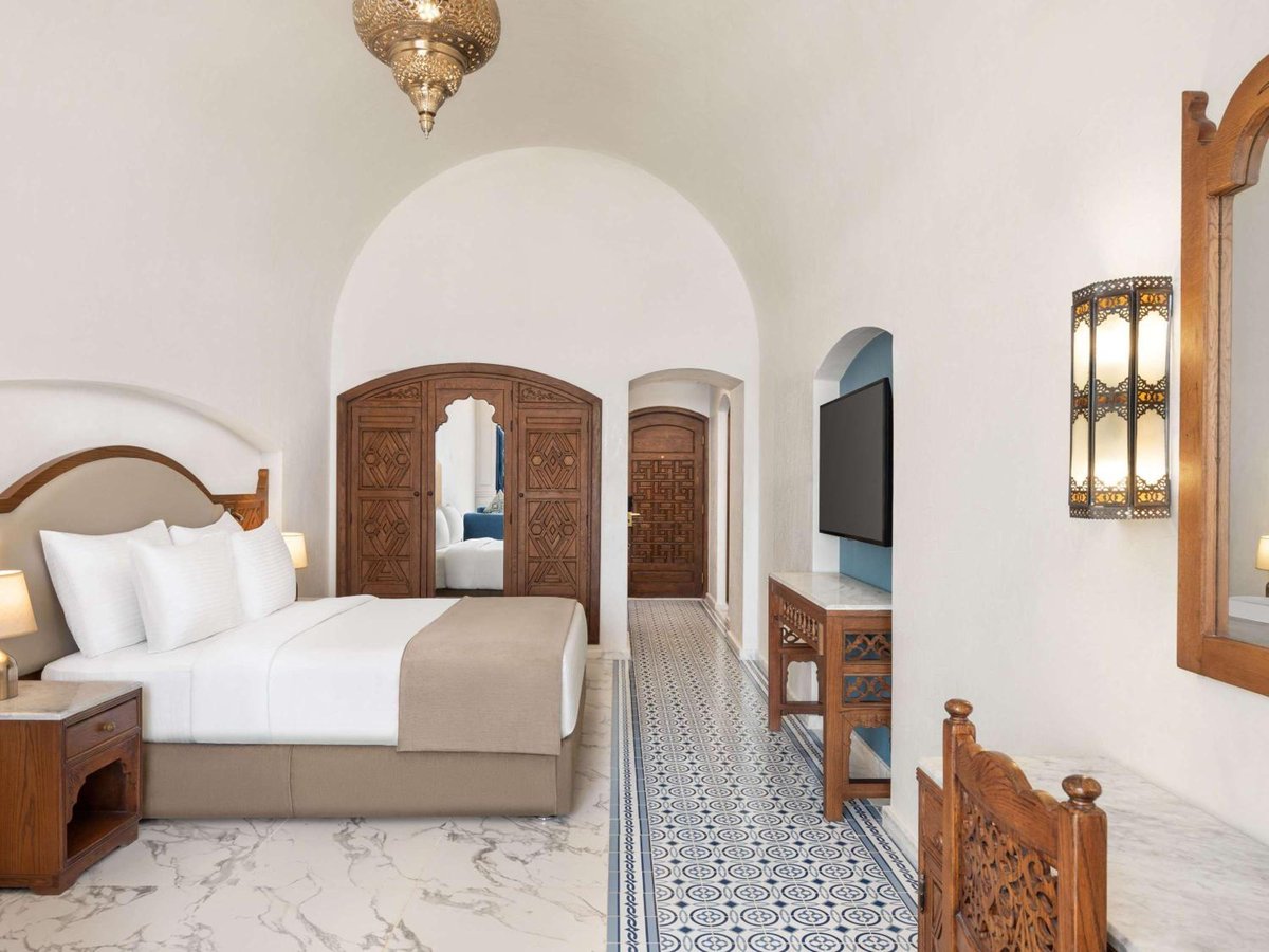 Movenpick Resort Sharm El Sheikh bedroom with a carved wooden bed frame and patterned tile floor.