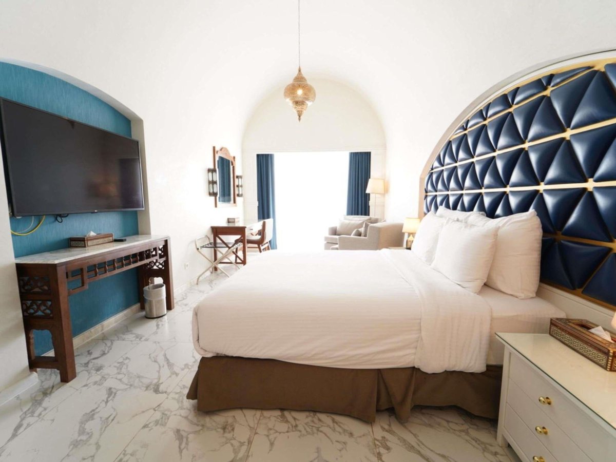 Movenpick Resort Sharm El Sheikh guest bedroom with a king bed and a navy tufted headboard.