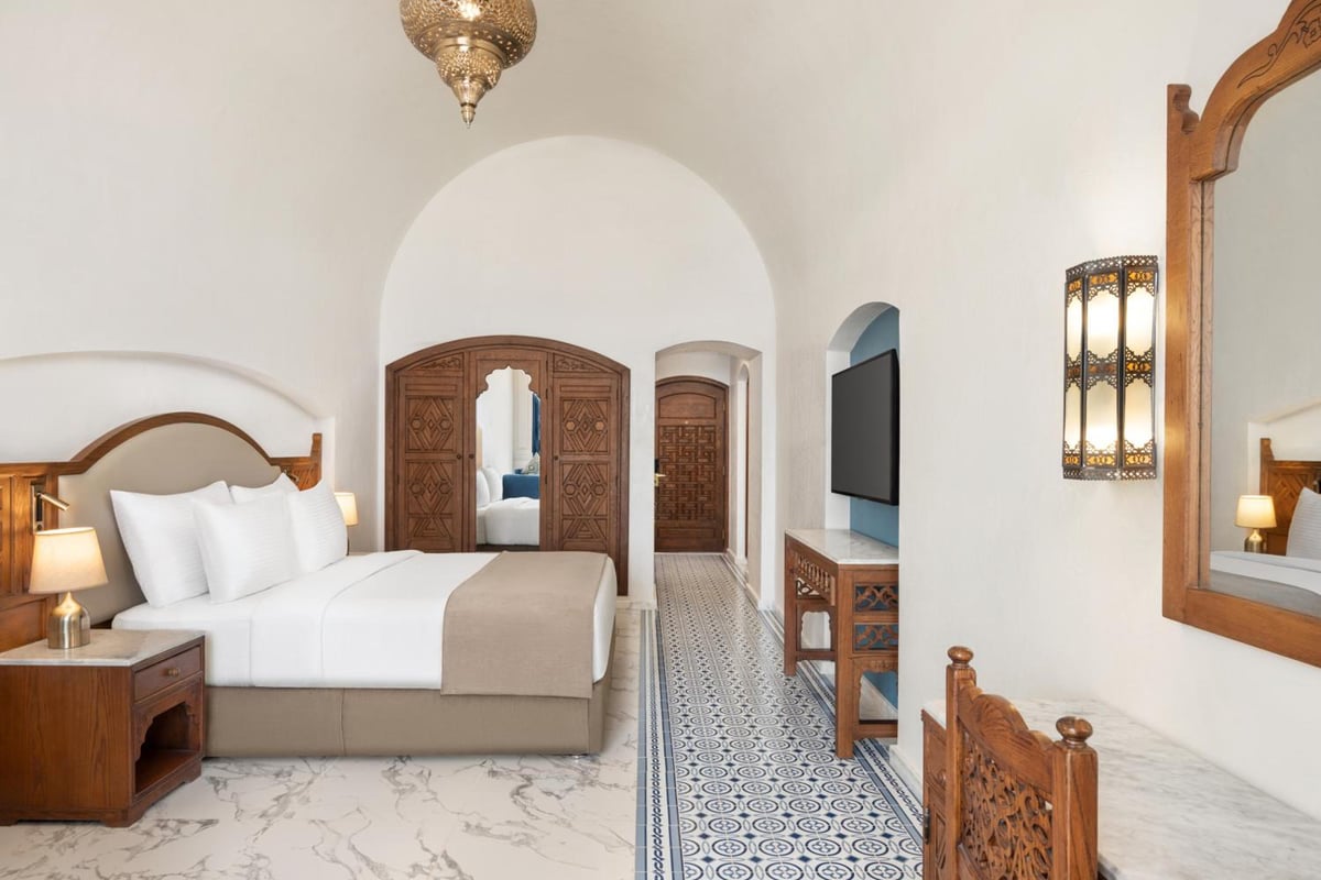 Movenpick Resort Sharm El Sheikh bedroom with a carved wooden bed and patterned tile floor.