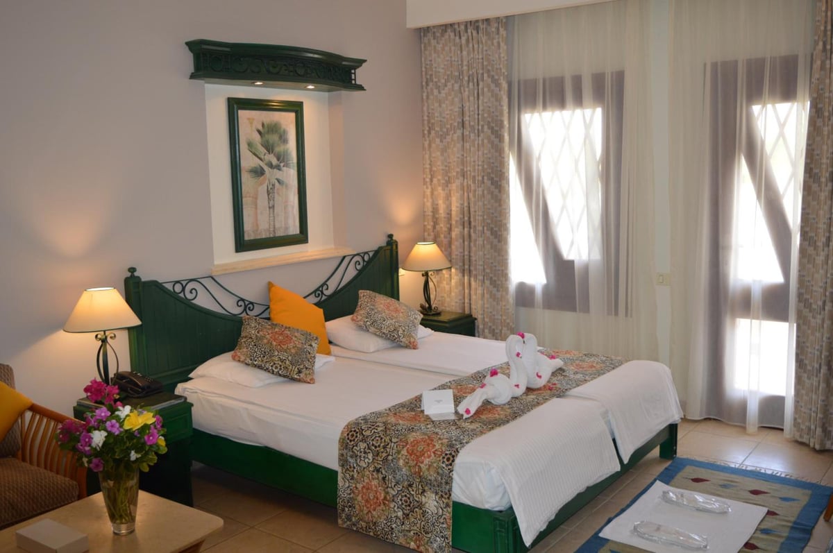 Swiss Inn Resort Dahab guest bedroom with a green metal headboard and sheer curtains.
