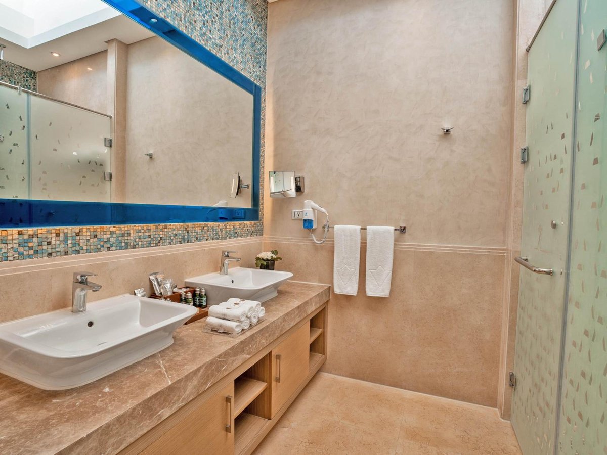 Rixos Premium Magawish Suites & Villas bathroom with double sinks and a glass shower enclosure.