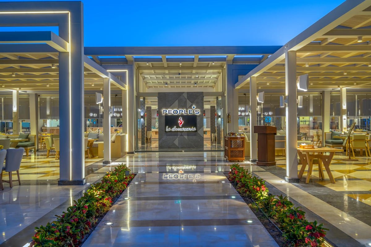 Rixos Premium Magawish Suites & Villas restaurant entrance with pergola dining areas and flower-lined walkway.