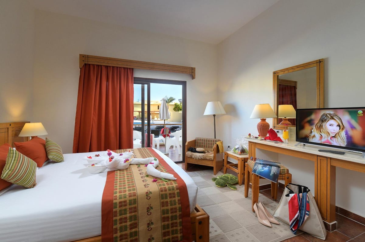 Three Corners Fayrouz Plaza Beach Resort bedroom with a made bed and sliding glass doors.