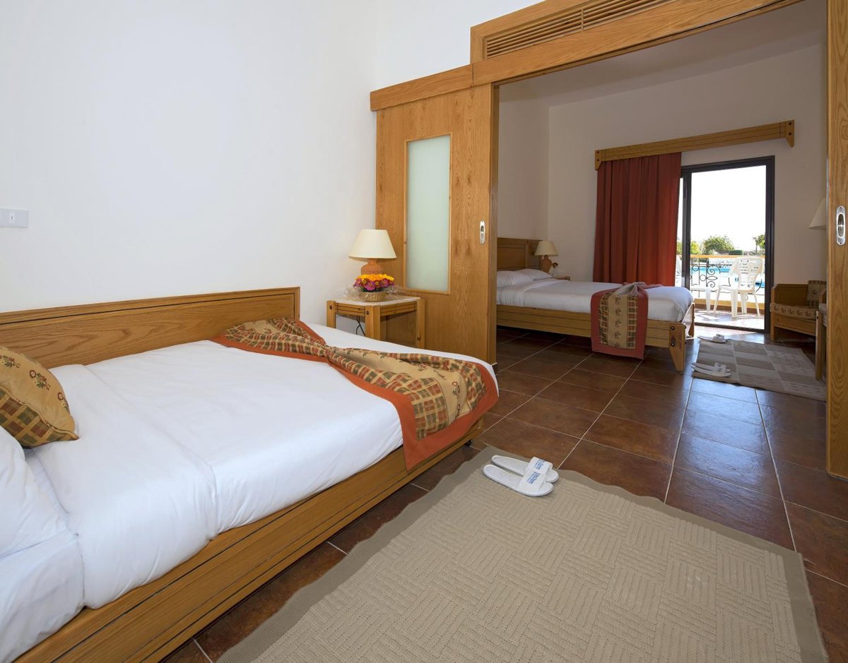 Three Corners Fayrouz Plaza Beach Resort guest bedroom with a wooden bed and tiled floor.