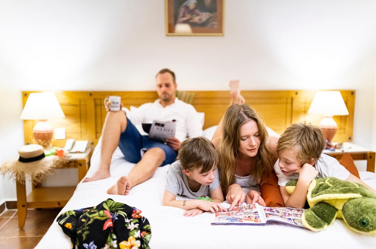 Three Corners Fayrouz Plaza Beach Resort bedroom with a wooden headboard and family reading on the bed.