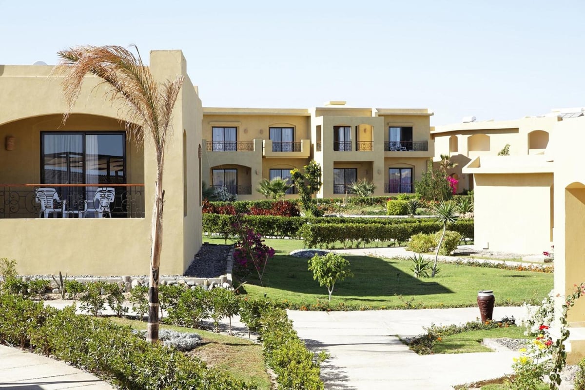 Three Corners Fayrouz Plaza Beach Resort garden courtyard with a green lawn and tan buildings.
