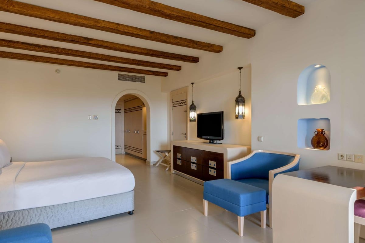Hilton Marsa Alam Nubian Resort bedroom with wooden ceiling beams and a blue armchair.