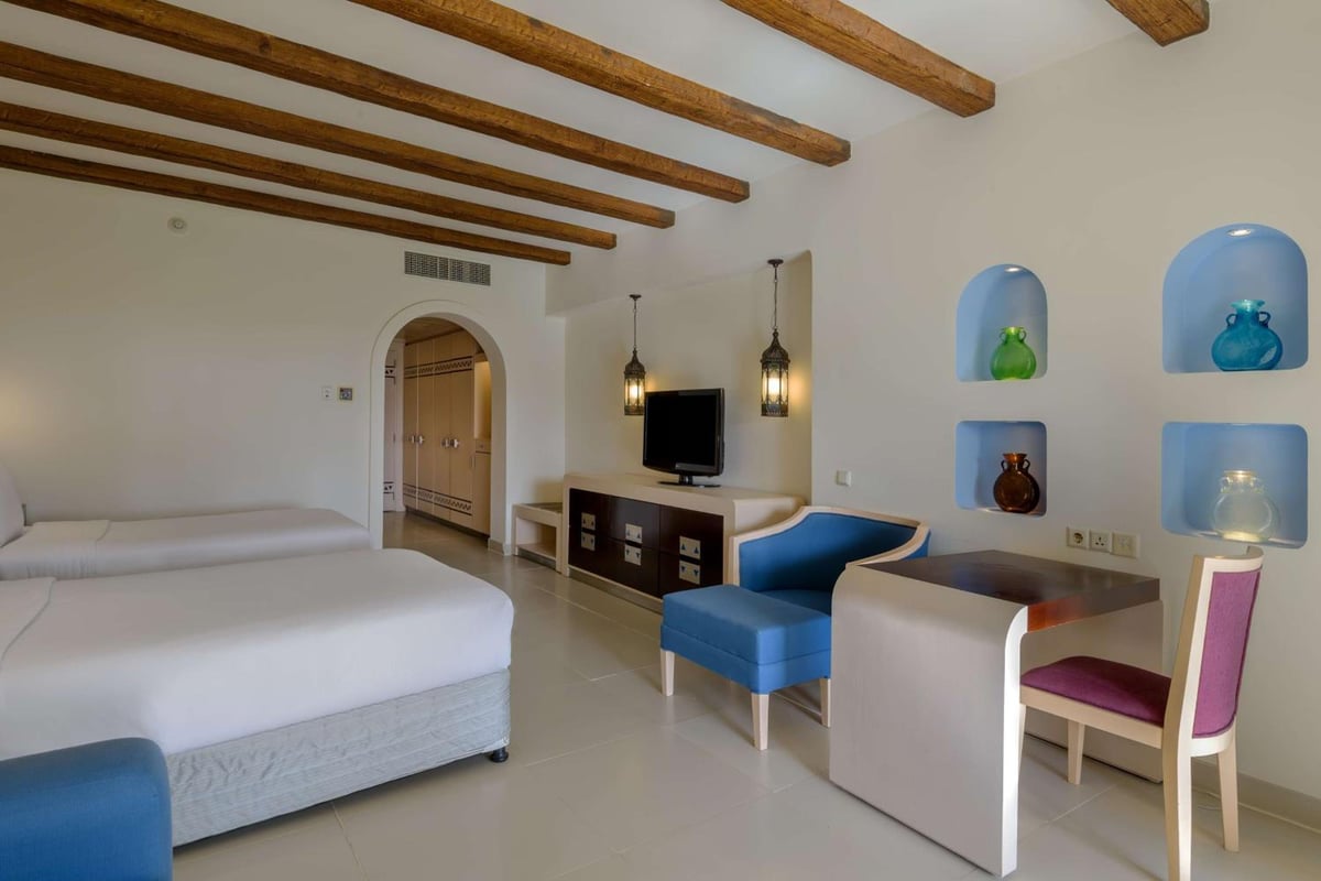Hilton Marsa Alam Nubian Resort guest room with wooden ceiling beams and blue seating.
