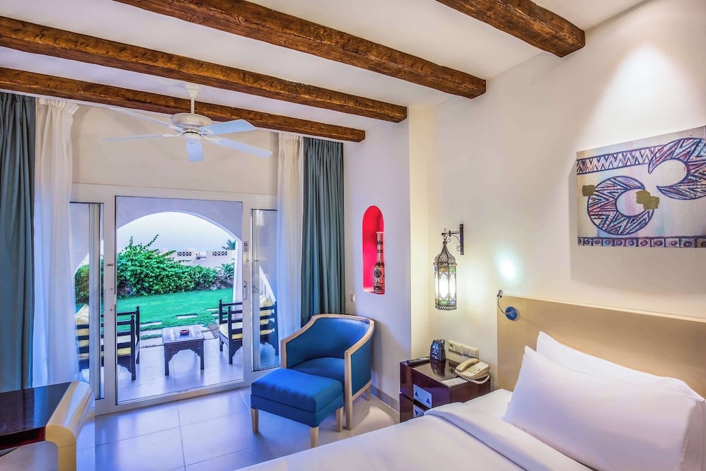 Hilton Marsa Alam Nubian Resort guest room with exposed ceiling beams and doors to a terrace.