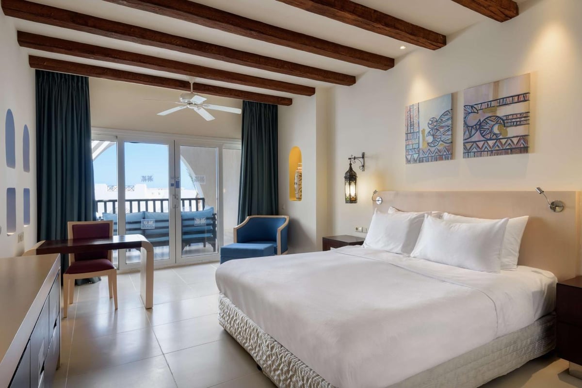 Hilton Marsa Alam Nubian Resort bedroom with a white bed and exposed wooden ceiling beams.