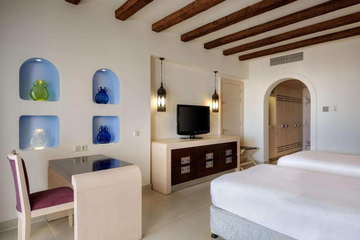Hilton Marsa Alam Nubian Resort guest room with wooden ceiling beams and an arched doorway.