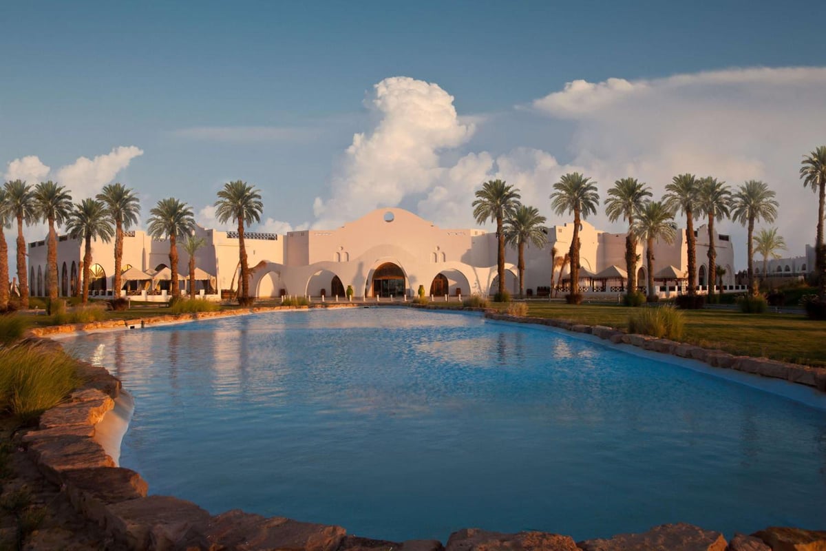 Hilton Marsa Alam Nubian Resort pool with palm trees and an arched entrance.