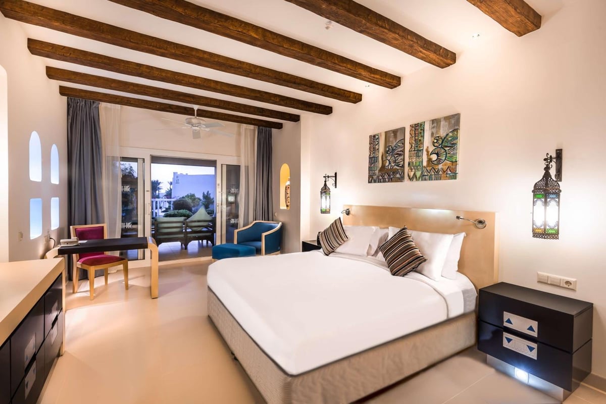Hilton Marsa Alam Nubian Resort guest bedroom with a large bed and exposed wooden ceiling beams.