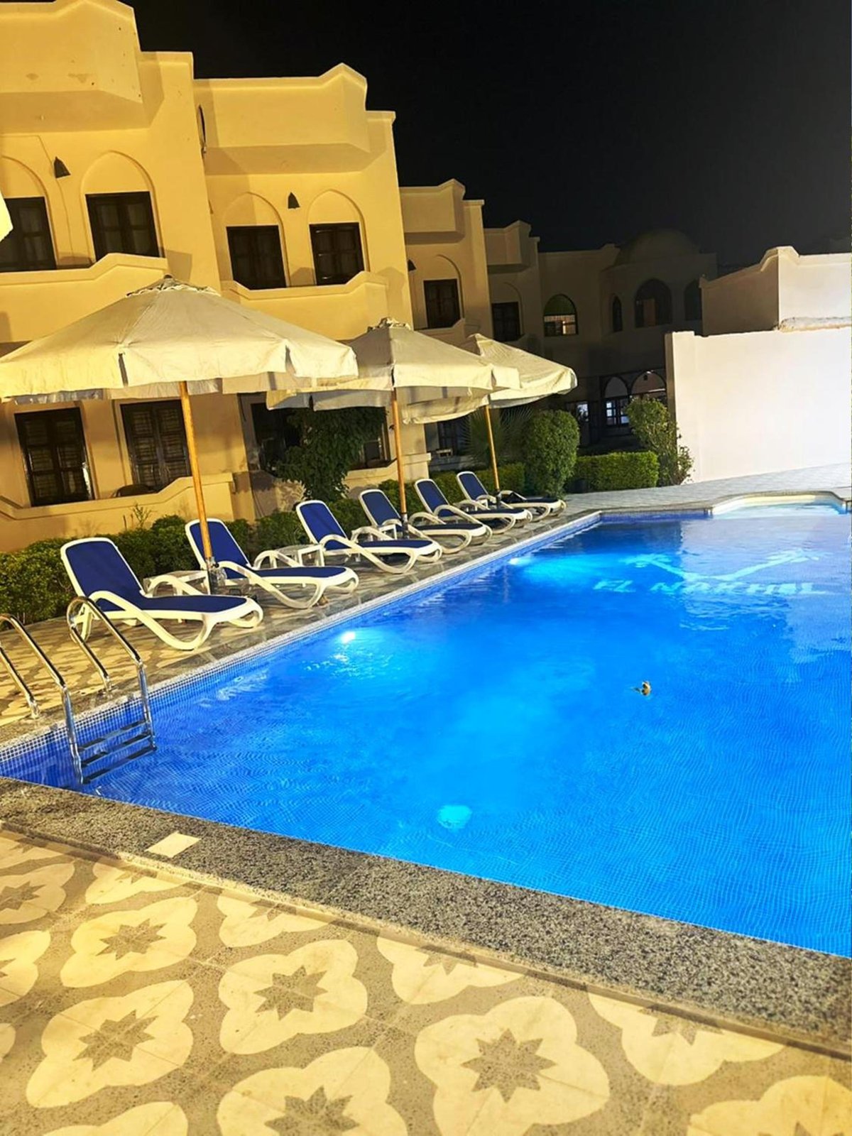 El Nakhil Hotel Luxor pool with blue-lit water and umbrella-shaded loungers.