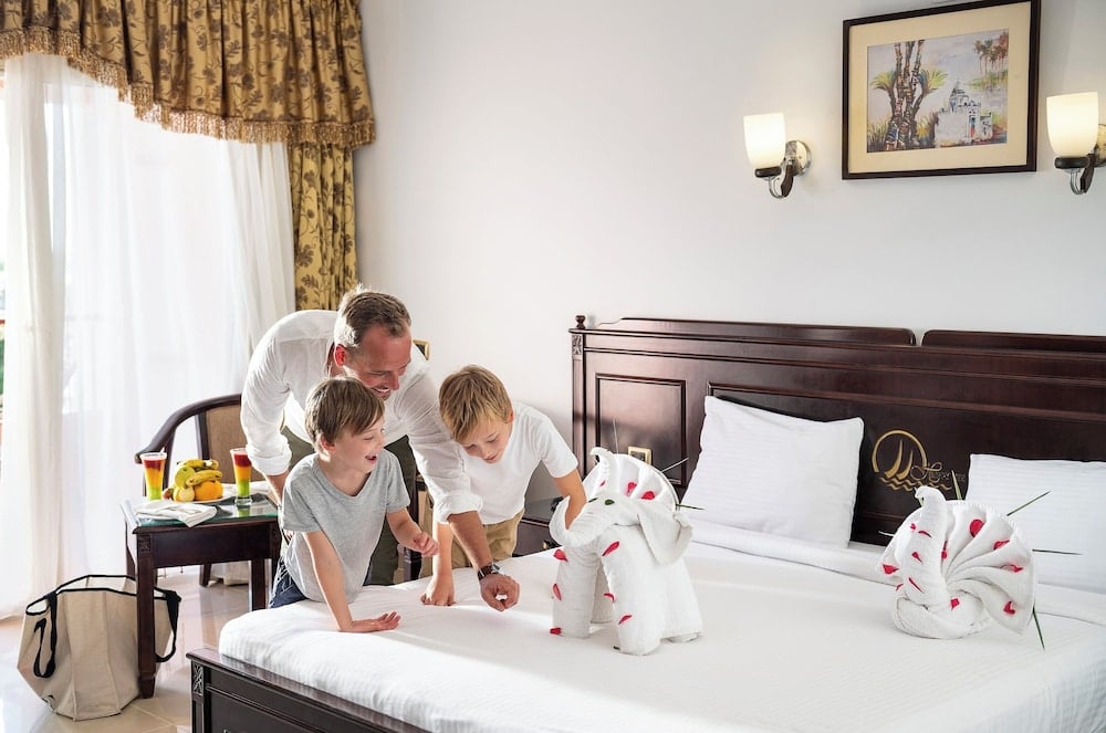 Three Corners Happy Life Beach Resort bedroom with a white bed and dark wood headboard.