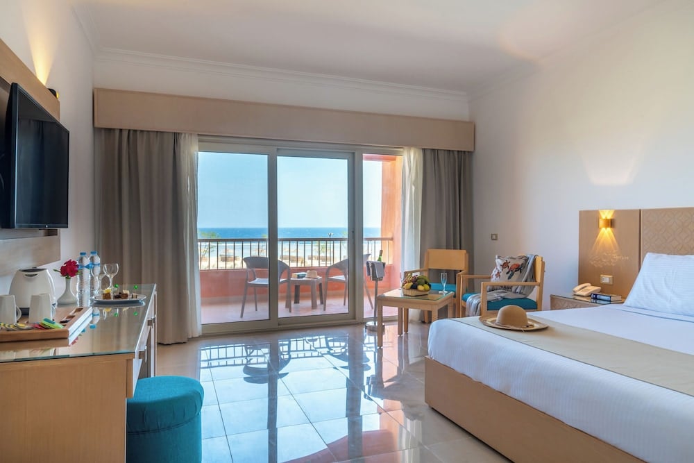 Three Corners Happy Life Beach Resort bedroom with a large bed and a balcony overlooking the sea.