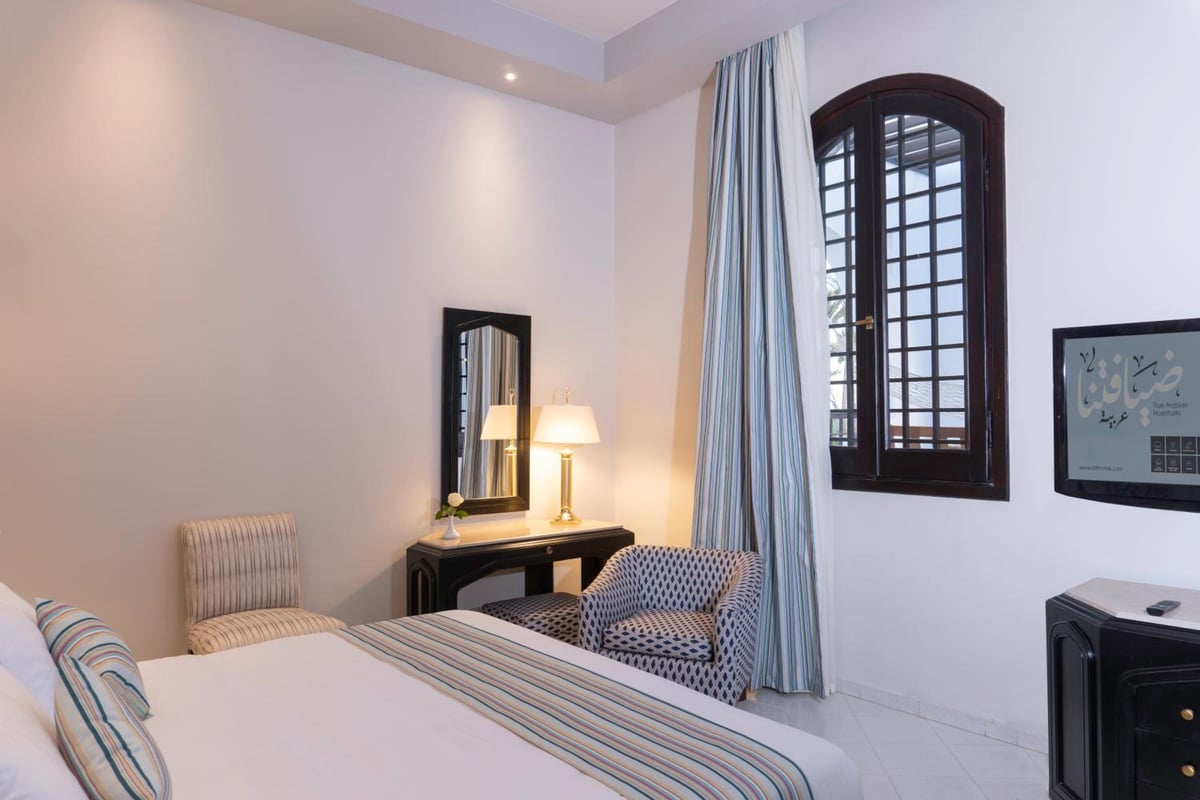Safir Dahab Resort guest room with a striped bed and an arched window.
