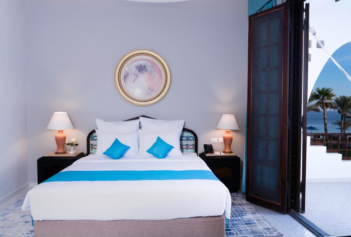 Safir Dahab Resort bedroom with a white bed and a sea view through an open door.