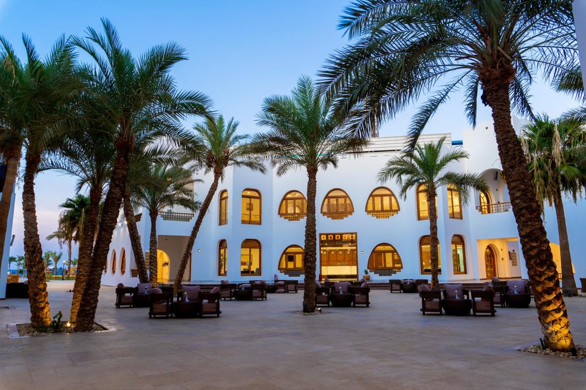 Safir Dahab Resort courtyard with palm trees and arched windows.